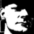 Pixelated black-and-white icon of a stylized face with exaggerated features, including large eyes and a prominent nose, against a solid dark background.