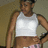 Pixelated image of a person wearing a white tank top and pink-patterned shorts, standing with one hand on hip against a muted brown background.