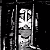 Black-and-white pixelated image of a person with long hair making a peace sign gesture, standing behind vertical bars.