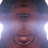 Pixelated static image of a person's face with dark hair, brown skin tone, and visible eyes and mouth against a light purple gradient background.