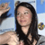 A pixelated static image shows a person with long dark hair wearing a black top, with a blurred background featuring blue and light tones.