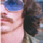 Pixelated static image of a person's face with blue hair and dark clothing against a blurred background.