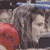 Pixelated static image of a person with light skin and dark hair, wearing a red garment on the left side, against a blurred background with blue and gray tones.