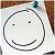 A pixelated circular icon with a simple smiling face, featuring two small black dots for eyes and a curved line for a mouth, set against a light background with blurred brown and green elements.