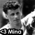 Black-and-white pixelated image of a person with dark hair and light clothing, featuring text reading 'Mino' in the lower-left corner.