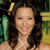 A pixelated portrait of a person with long dark hair, wearing a light-colored top, against a blurred green and yellow background.