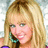Pixelated close-up of a person with long blonde hair holding a microphone, wearing a teal and black garment against a light background.