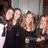 Four pixelated figures in dark clothing pose closely together against a blurred background with light and brown tones.