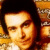 Pixelated static image of a person's face with warm orange and brown tones, dark hair, and visible facial features including eyes, nose, and mouth against a blurred background.