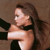 Pixelated image of a person with long brown hair wearing a dark sleeveless top, arms crossed, against a brown background.