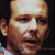 Static pixelated close-up of a bald man's face with light skin tone, visible facial features including eyes, nose, mouth, and ear, against dark background.