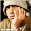 Pixelated static image of a person with long brown hair wearing a light-colored hooded jacket and white beanie, covering their face with one hand in a distressed pose against dark background.