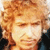 Pixelated close-up of a person with light brown curly hair, closed eyes, and a neutral expression against a dark background.