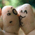 Two cartoon-style characters with light brown skin and black hair kiss on the lips, set against a blurred green background.
