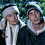 Three figures in period-style clothing with white collars and hats, positioned against a green background.