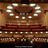 Pixelated image of a theater interior with rows of seats, a stage, and a decorative proscenium arch with illuminated elements.
