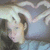 A person with light hair lies on a blue surface, forming a heart shape with their hands above their head in