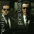 Pixelated figure in dark suit with white shirt and tie, holding a gun, standing against dark background with partial text elements.