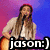 A person with long brown hair plays an acoustic guitar on a stage with purple and blue background, wearing a light-colored cardigan over a white top.