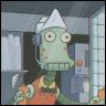 Green-skinned cartoon character with large eyes, wearing a white chef's hat and orange apron, standing in a kitchen with cabinets and appliances.