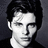 Pixelated grayscale portrait of a person with dark hair, neutral expression, and visible ear against dark background.