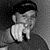 A grayscale pixelated image of a person with short dark hair wearing a light-colored shirt, captured in two showing slight head movement