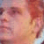 Pixelated close-up of a person's face with warm skin tones and reddish-brown hair, showing partial facial features against a light background.