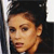 A pixelated close-up of a person's face with light brown hair, dark eyes, and a neutral expression, set against a dark background with a vertical light stripe on the left.