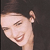 Pixelated close-up of a smiling person with closed eyes, dark hair, and a dark background.