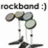 Pixelated image showing a drum set with three cymbals and two drums, accompanied by text reading 'rockband :)' above the instruments.