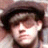 Pixelated close-up of a person's face with dark hair, light skin, and a neutral expression against a blurred background.