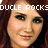 Pixelated close-up of a person with brown hair and light skin, overlaid with white pixelated text reading "DOUCLE ROCKS" across the top.