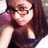 Pixelated image of a person with long brown hair wearing dark clothing and glasses, smiling slightly against a light background.