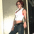 Pixelated image of a person in a white sleeveless top and dark pants standing against a light background with vertical elements.