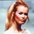 Pixelated close-up of a person with light brown hair tied back, wearing a white top against a light blue background.