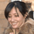 A pixelated close-up of a person with short dark hair smiling, wearing a light brown jacket against a blurred background.