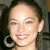 A pixelated close-up of a person's face with dark hair pulled back, wearing large hoop earrings and a light-colored top.