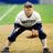 A pixelated softball player in a crouched stance on a field with green grass and blue sky, next to bright yellow background with green text reading "Softball is LIFE".
