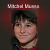 A static portrait of a person with short dark hair and a red shirt, with text reading "Mitchel Musso" above the head against a dark red gradient background.