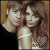 Static pixelated image of two people in close proximity with brown hair and light-colored clothing against a gradient background.
