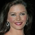 A static pixelated image shows a person with dark hair, light skin, and a smiling expression against a dark background.