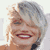 Pixelated static image of a person with short light-colored hair and red lipstick smiling, wearing dark clothing against a plain background.