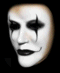 White face with black tear-like marks under eyes, dark lips, and a subtle smile against varying backgrounds.