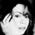 Pixelated grayscale image of a person with light skin tone holding a hand near their face, dark hair visible on the right side, black background.
