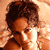 Pixelated static image of a person with curly hair and warm-toned skin against an orange background, rendered in low-resolution 50x50 pixels.