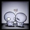 Two round-headed cartoon figures stand close together, one with a heart-shaped eye and the other with a closed eye, both holding small hearts, with a floating heart and exclamation mark above them.