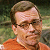 Pixelated static image of a person with short brown hair wearing glasses and an orange shirt against a blurred green background.