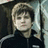 Pixelated static image of a person with light brown hair and dark clothing against a dark background with light vertical elements.