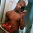 Pixelated image of a shirtless man with dark hair and beard holding a red object near his face against blurred background.