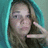 Pixelated image of a person with light brown hair wearing a teal hooded garment, making a peace sign with their right hand against a solid blue background.